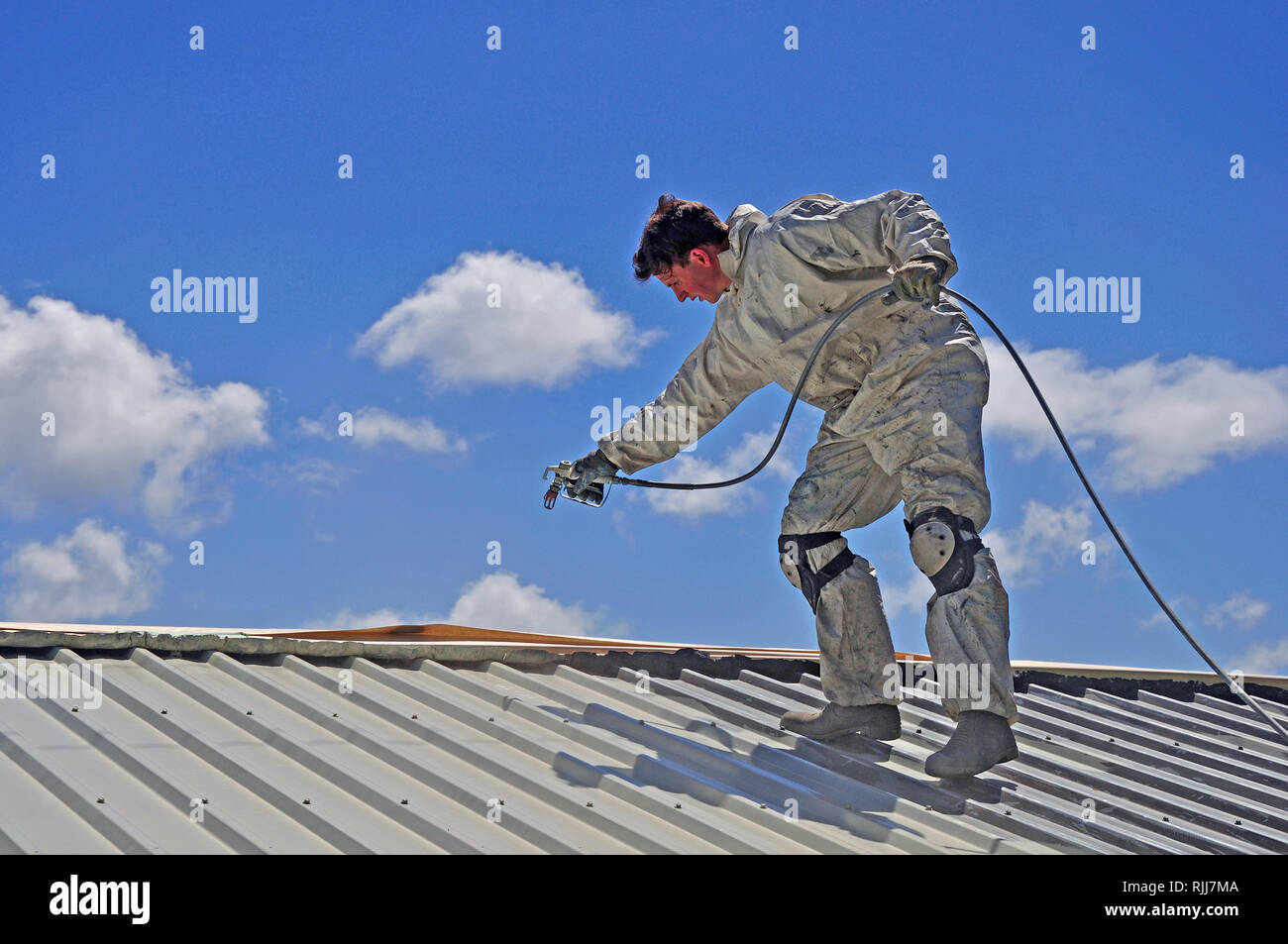 Un trademan utilizza un spruzzo airless per la verniciatura del tetto di un edificio Foto Stock