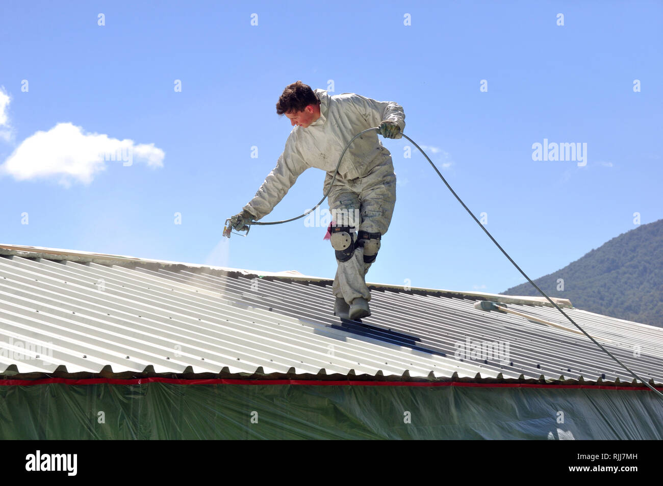 Un trademan utilizza un spruzzo airless per la verniciatura del tetto di un edificio Foto Stock