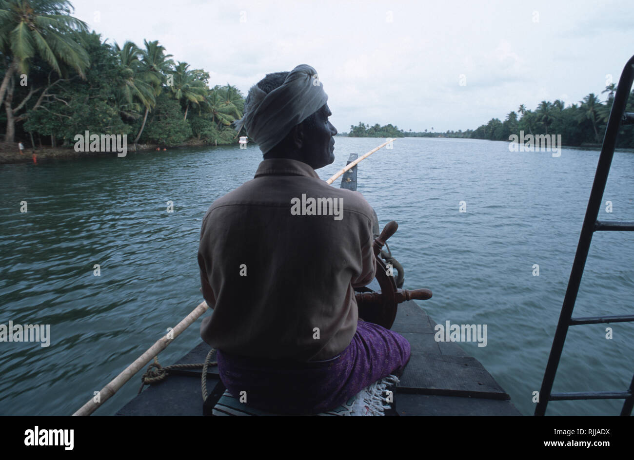 Il capitano di una casa galleggiante guida il suo vascello attraverso la miriade di acque secondarie del Kerala. Foto Stock