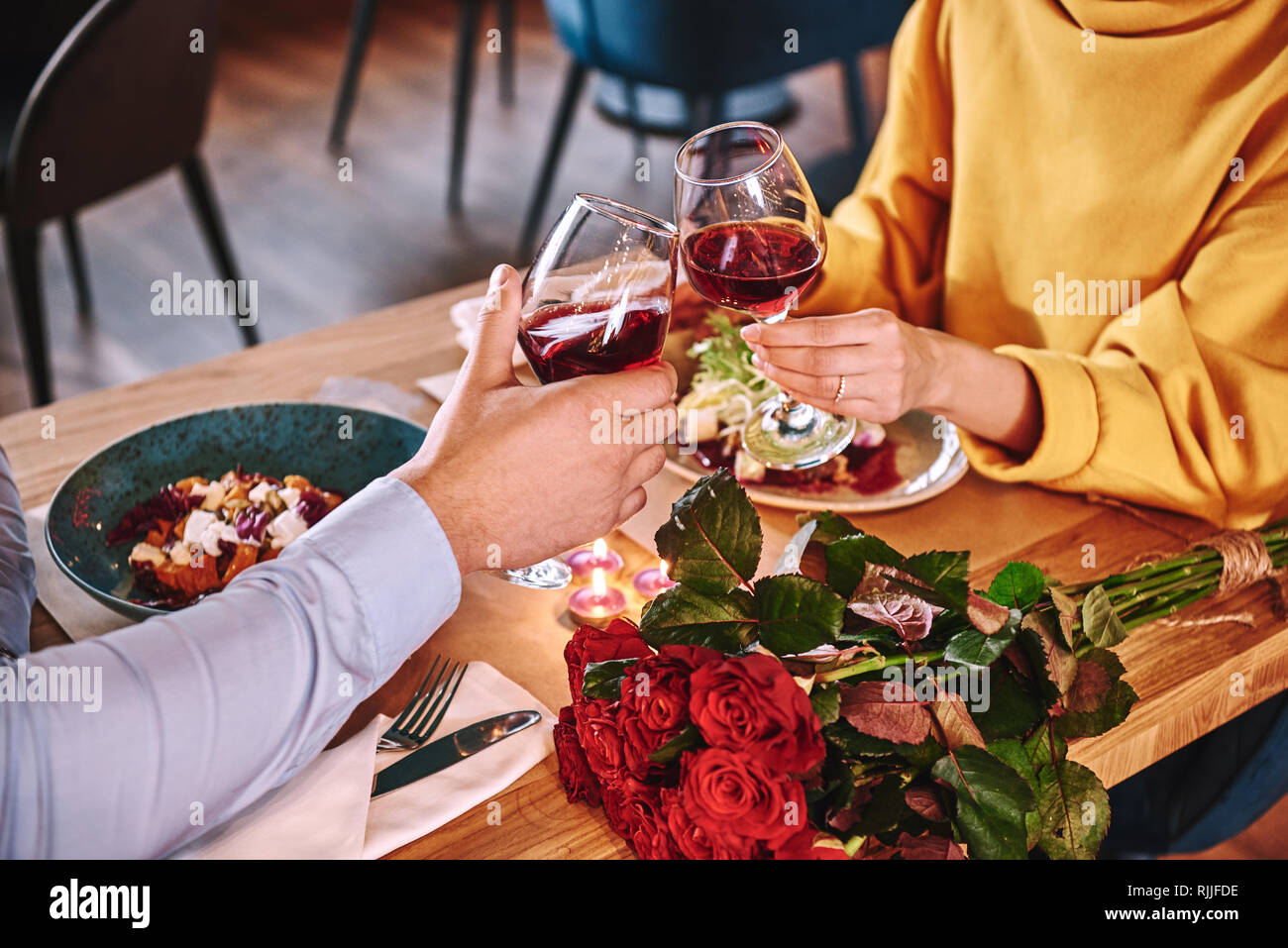 Momenti felici. Close-up del giovane azienda vino rosso in bicchieri nel ristorante. Rose rosse e candele sono giacenti sul tavolo vicino al vino rosso. Giovani wom Foto Stock
