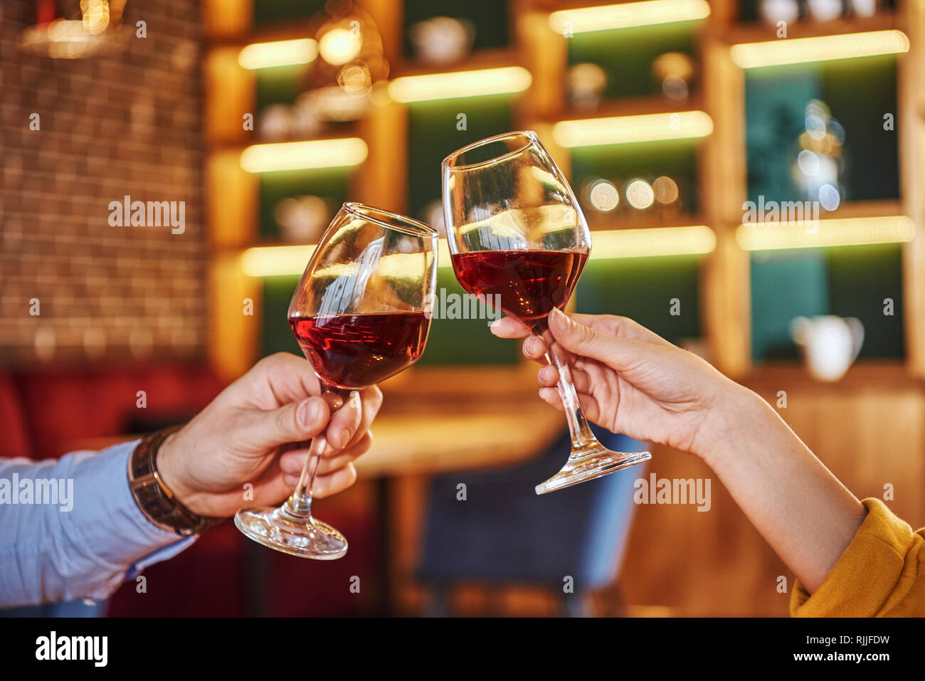 Due bicchieri insieme. Close-up del giovane azienda vino rosso in bicchieri nel ristorante. Rose rosse e candele sono giacenti sul tavolo vicino al vino rosso. Yo Foto Stock