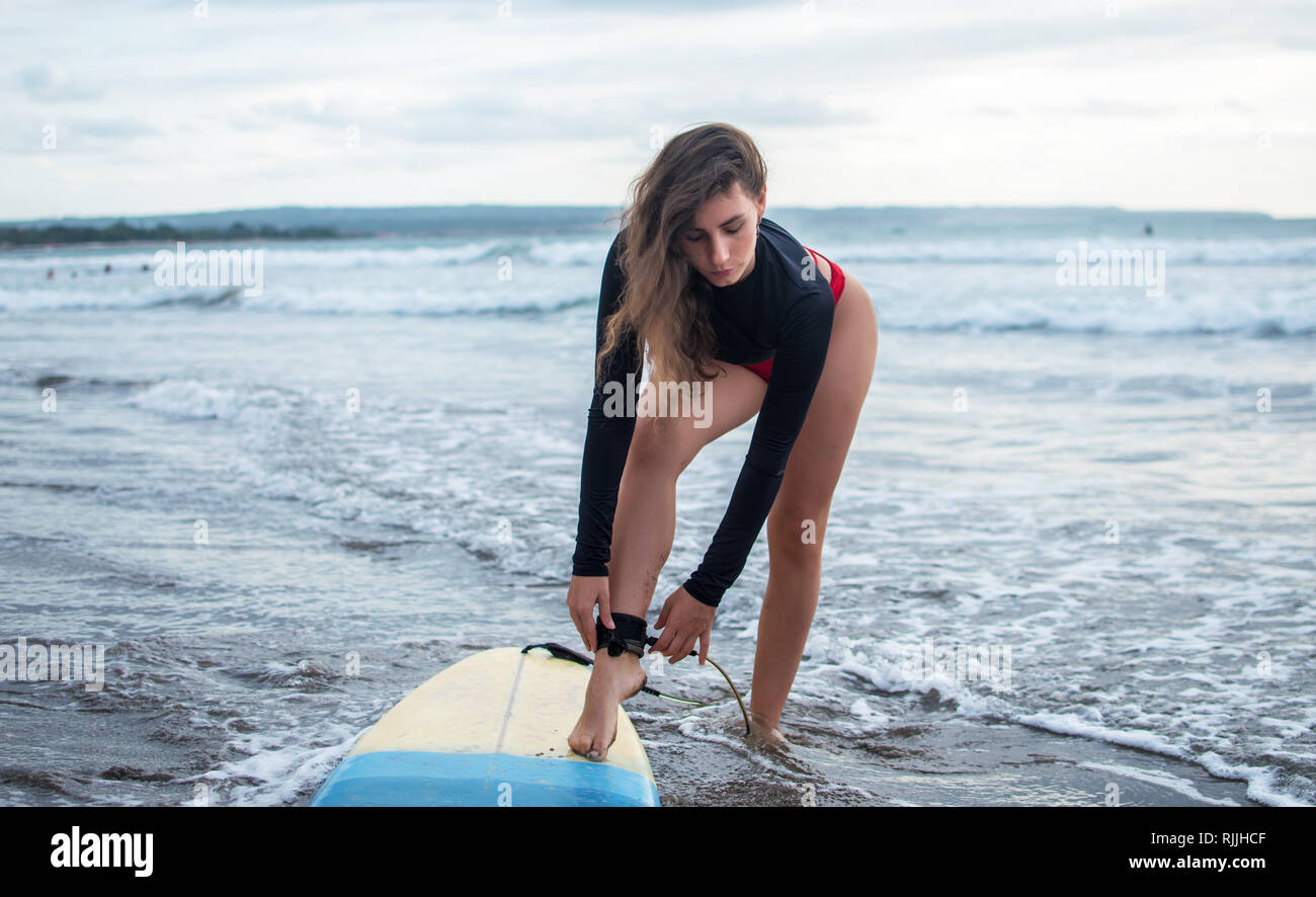 Unrecognizble a piedi nudi la donna ha fissato legrope, sorge sulla sabbia vicino a tavola da surf, protegge se stessa dal a schiantarsi sulla riva linee, ha uno stile di vita attivo Foto Stock