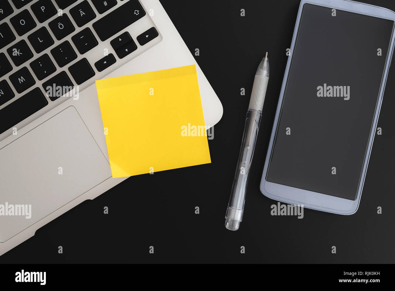 Nota adesiva sul computer portatile accanto a smart phone e penna su sfondo scuro Foto Stock