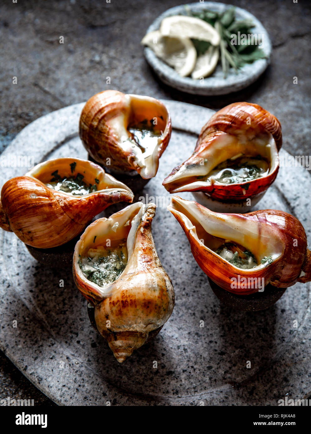 Cileno lumache giganti con burro e aglio ed erbe sulla pietra grigia piastra. escargot dall'oceano pacifico Foto Stock