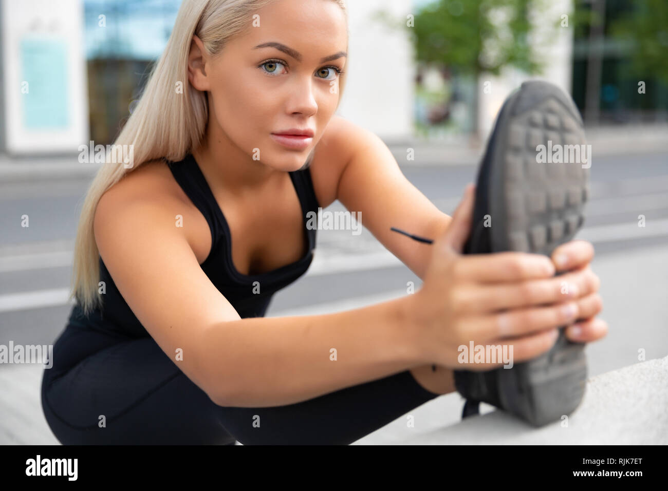 Sorridente stupendo giovane donna facendo esercizio di stiramento al marciapiede in città Foto Stock