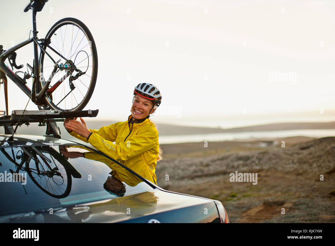 Sorridente giovane donna di attaccare la sua bicicletta per il tetto della sua automobile. Foto Stock