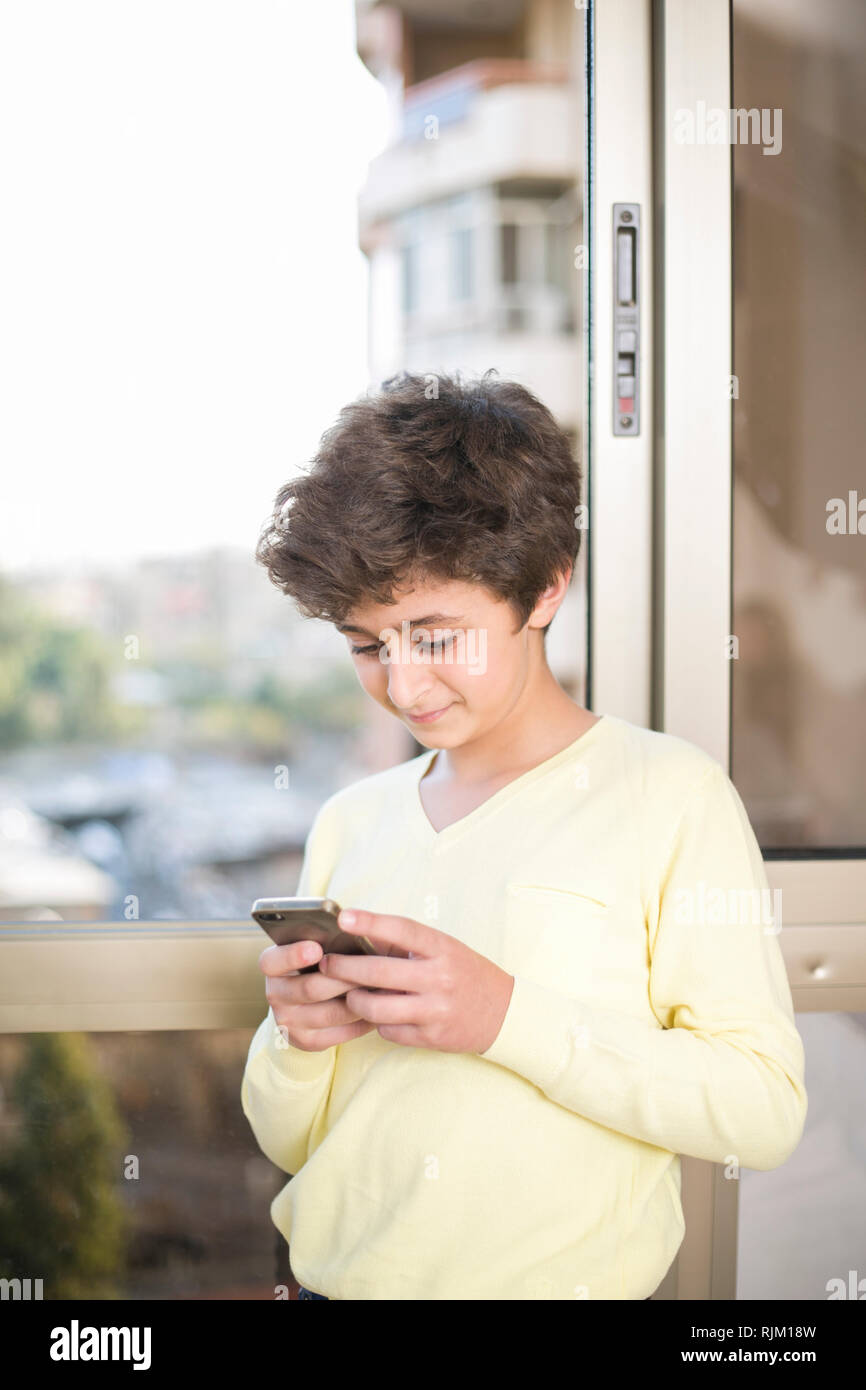 Boy utilizzando mobile smartphone mediante la finestra Foto Stock