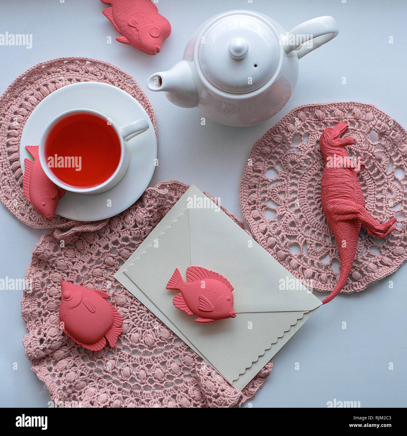 Wonderland surrealista di bere il tè - una tazza con aromatizzato tè rosa, maglia di tovaglioli, una teiera, giocattoli - pesce e dinosauro Foto Stock