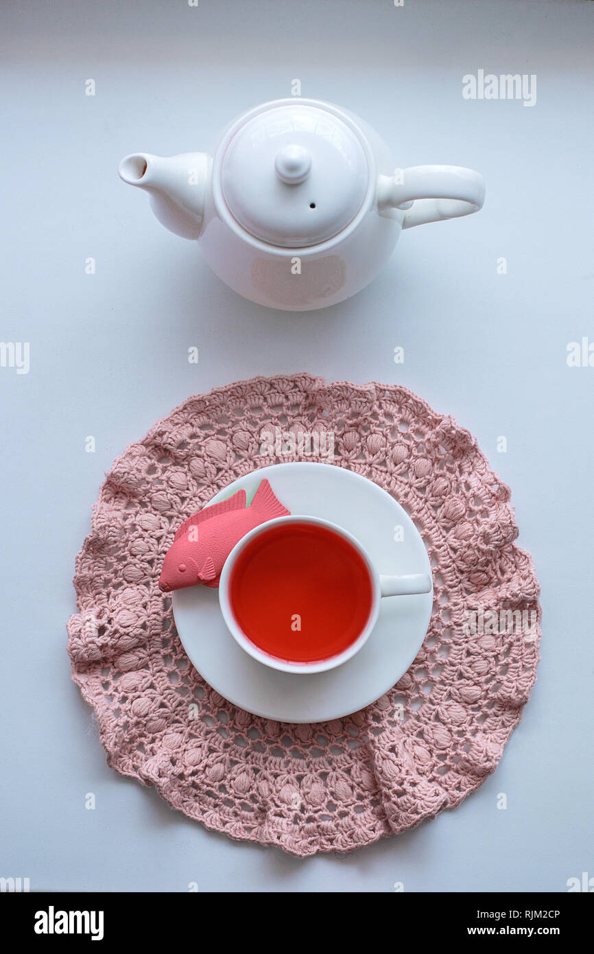 Wonderland surrealista di bere il tè - una tazza con aromatizzato tè rosa, maglia di tovaglioli, una teiera, giocattoli - pesce e dinosauro Foto Stock