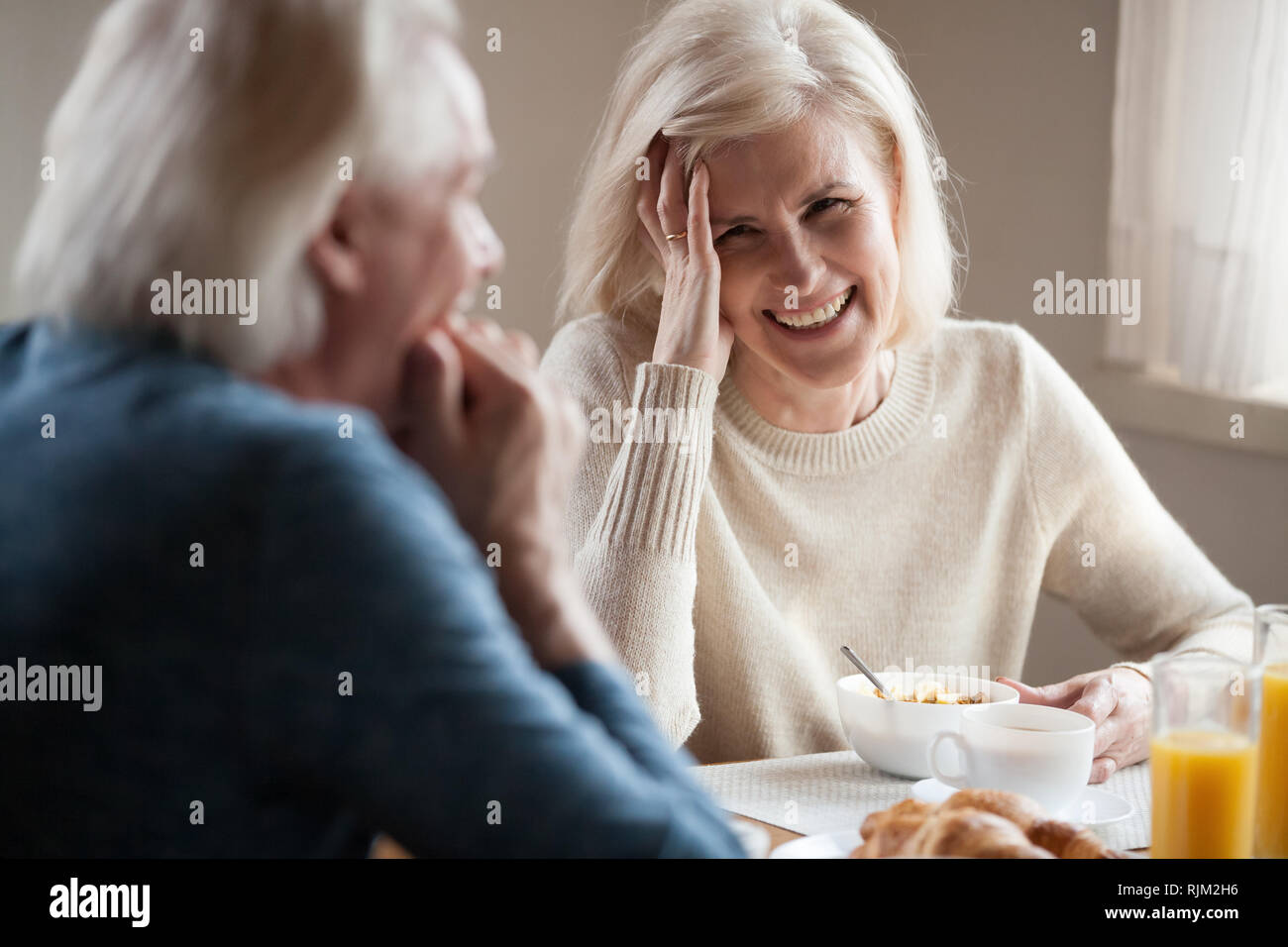 Capelli grigi coppia senior di ridere seduti al tavolo per la cena Foto Stock