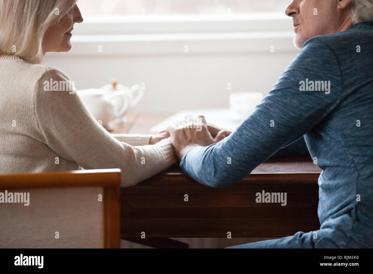 Immagine ritagliata coppia di mezza età seduta a tavola tenendo le mani Foto Stock