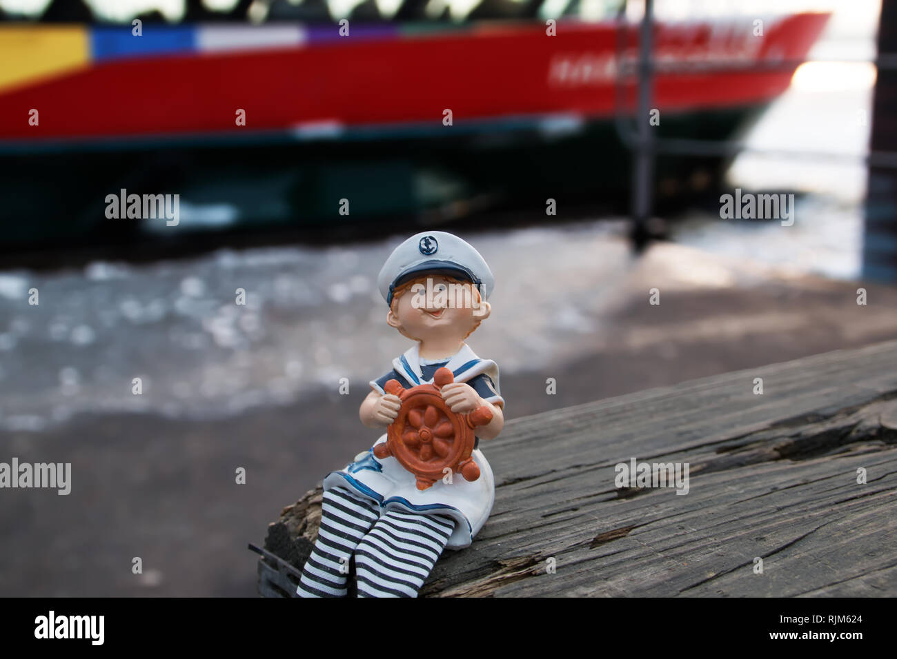 Un piccolo giovane marinaio figura è seduta sul molo e tenendo una ruota i bracci Foto Stock