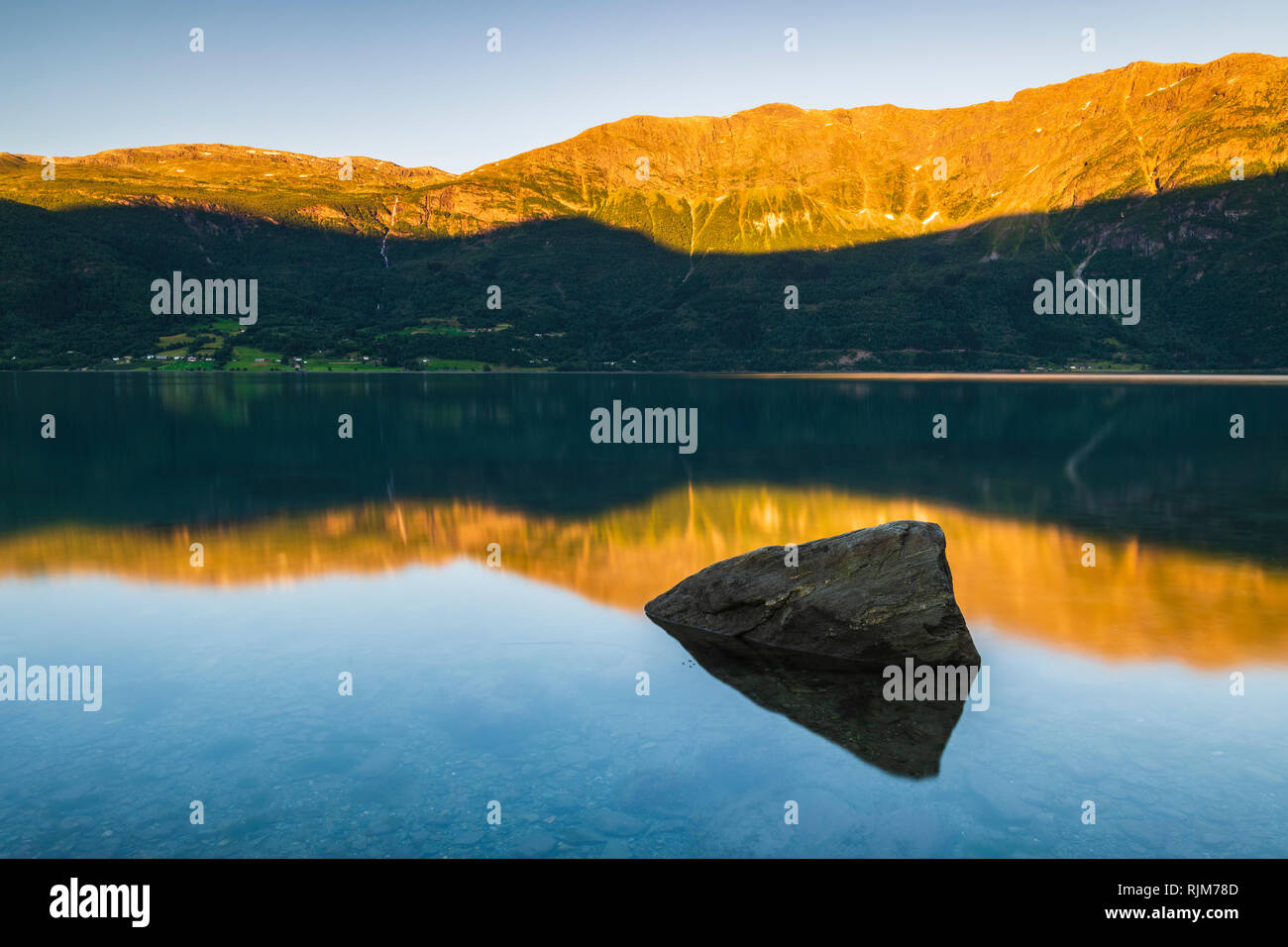 Formazione di grande roccia nel fiume calmo, montagne soleggiate in background, Lusterfjord, Norvegia, Europa Foto Stock