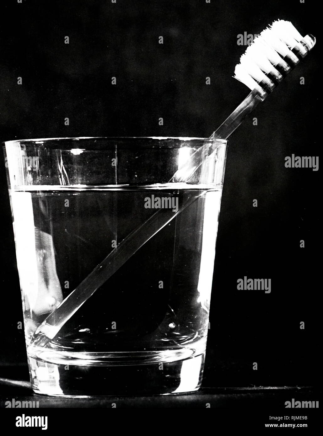 Rifratto immagine di una impugnatura dello spazzolino da denti come si vede in un bicchiere di acqua Foto Stock