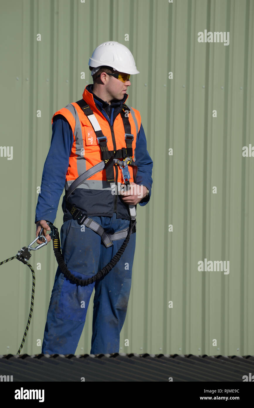 Un costruttore che indossa una imbracatura di sicurezza mentre si lavora ad altezze attende istruzioni dal caposquadra Foto Stock