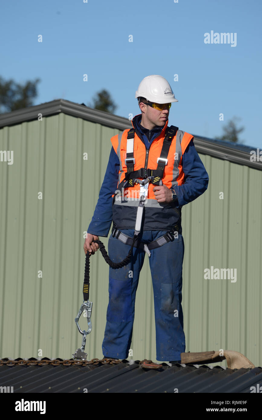 Un costruttore che indossa una imbracatura di sicurezza mentre si lavora ad altezze attende istruzioni dal caposquadra Foto Stock