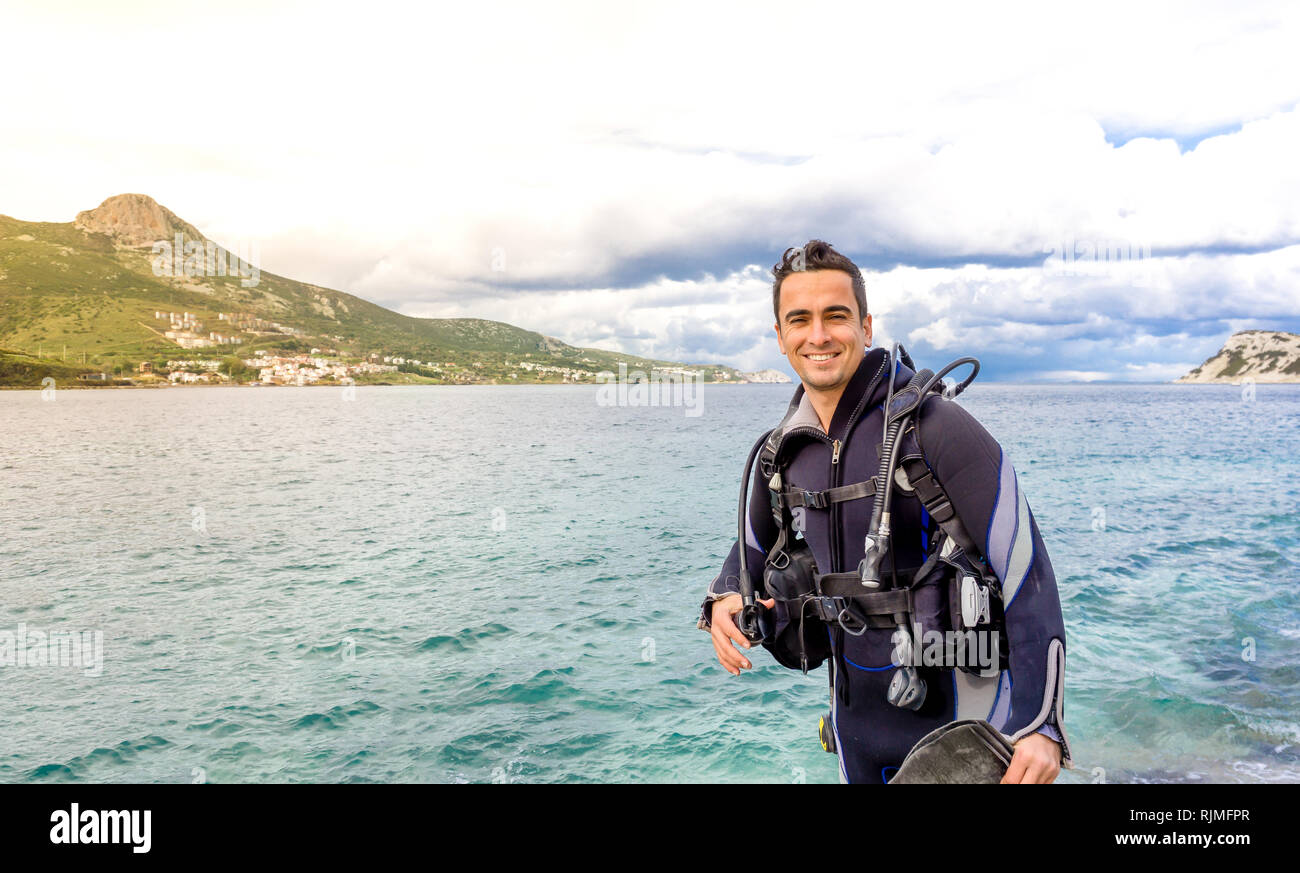 Giovane uomo bello diver sorridente pronto a fare immersioni in acqua fredda muta, alette, peso belt & oxigen ingranaggio in Karaburun, Izmir. Turchia Foto Stock