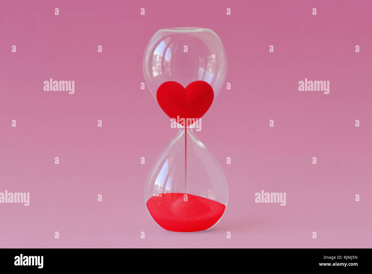 Cuore rosso che scorre nella clessidra su sfondo rosa - tempo per il concetto di amore Foto Stock