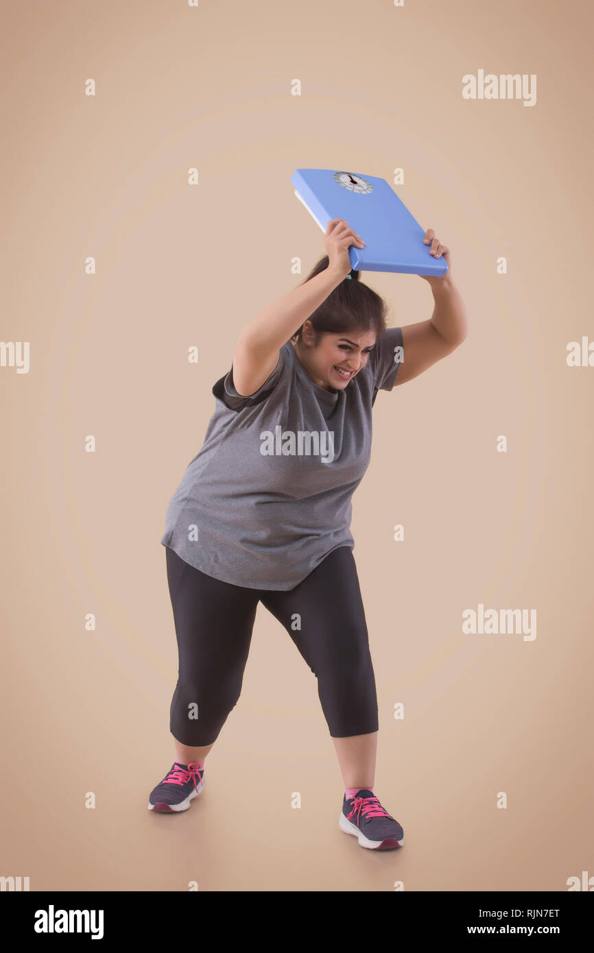 Adirato contro il sovrappeso donna frustrato dal suo peso scala di lancio Foto Stock