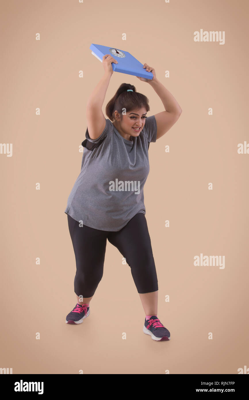 Adirato contro il sovrappeso donna frustrato dal suo peso scala di lancio Foto Stock