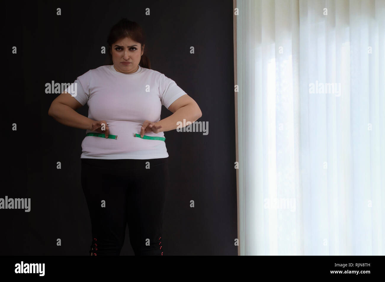 Donna sovrappeso misurando la sua vita con un nastro di misurazione Foto Stock