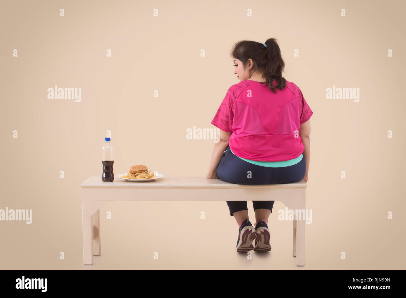 Il sovrappeso donna sta guardando la hamburger durante il riposo dopo allenamento Foto Stock