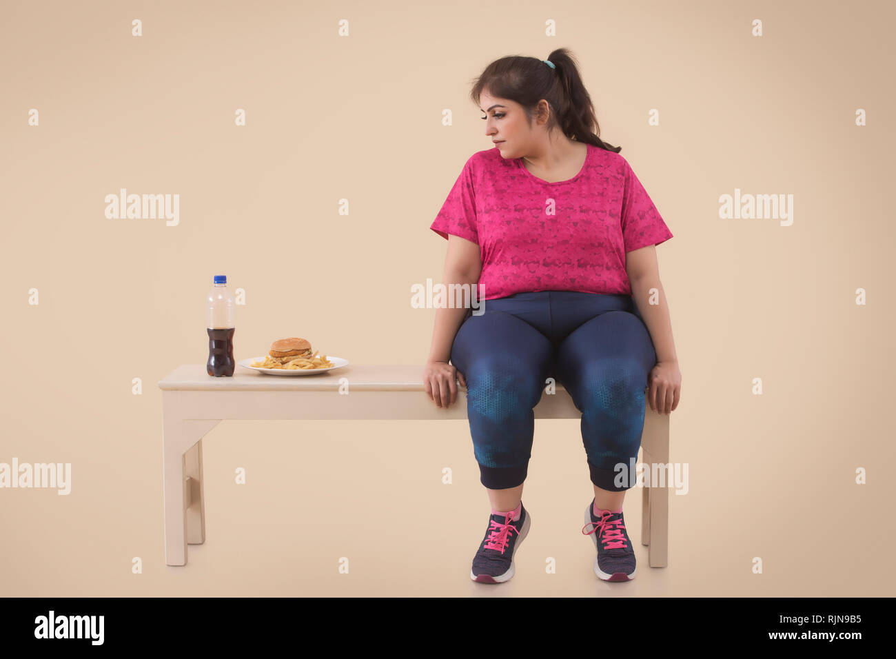 Il sovrappeso donna sta guardando la hamburger durante il riposo dopo allenamento Foto Stock