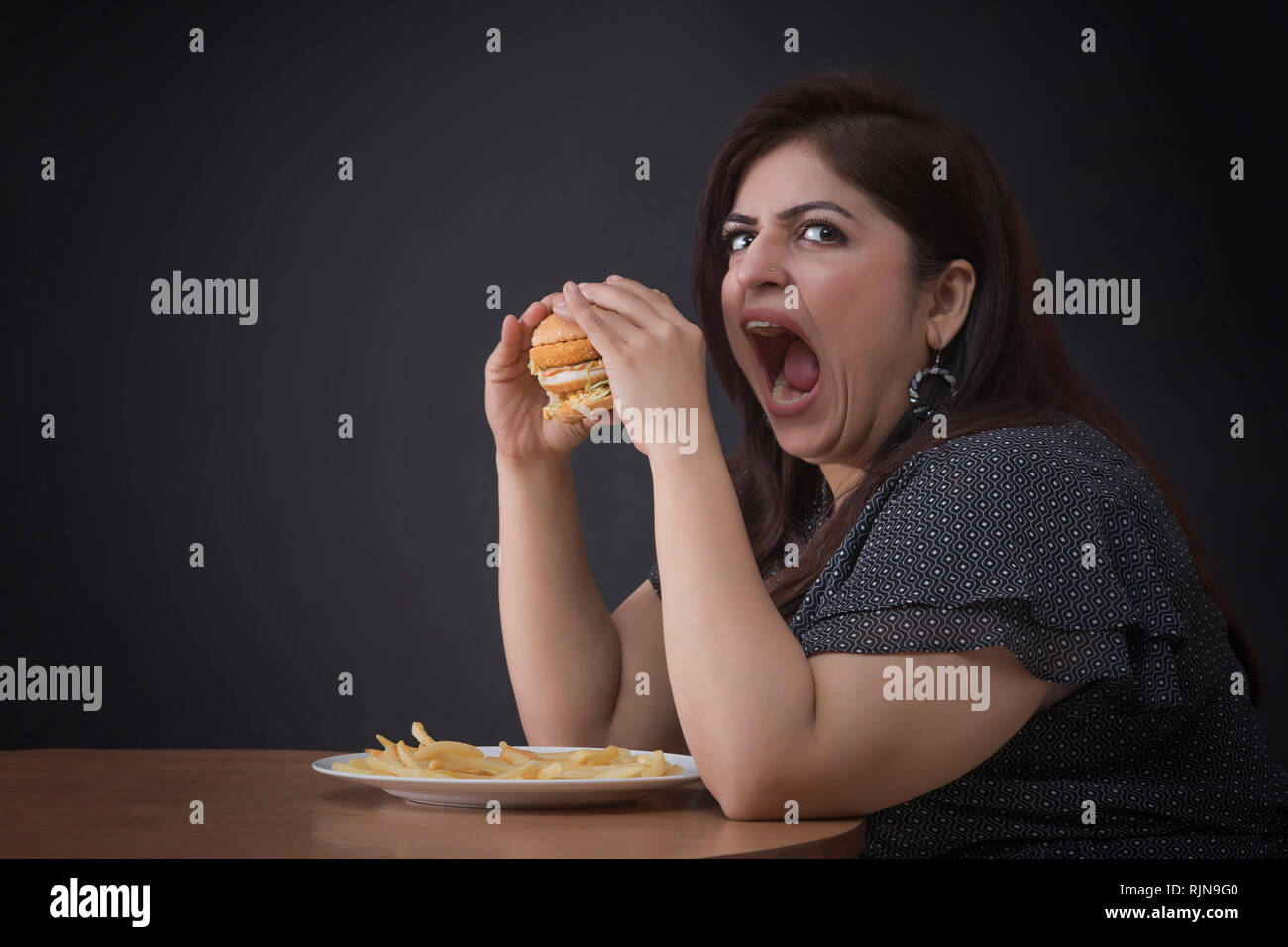 Arrabbiato irritato donna grassa mangiare un hamburger Foto Stock