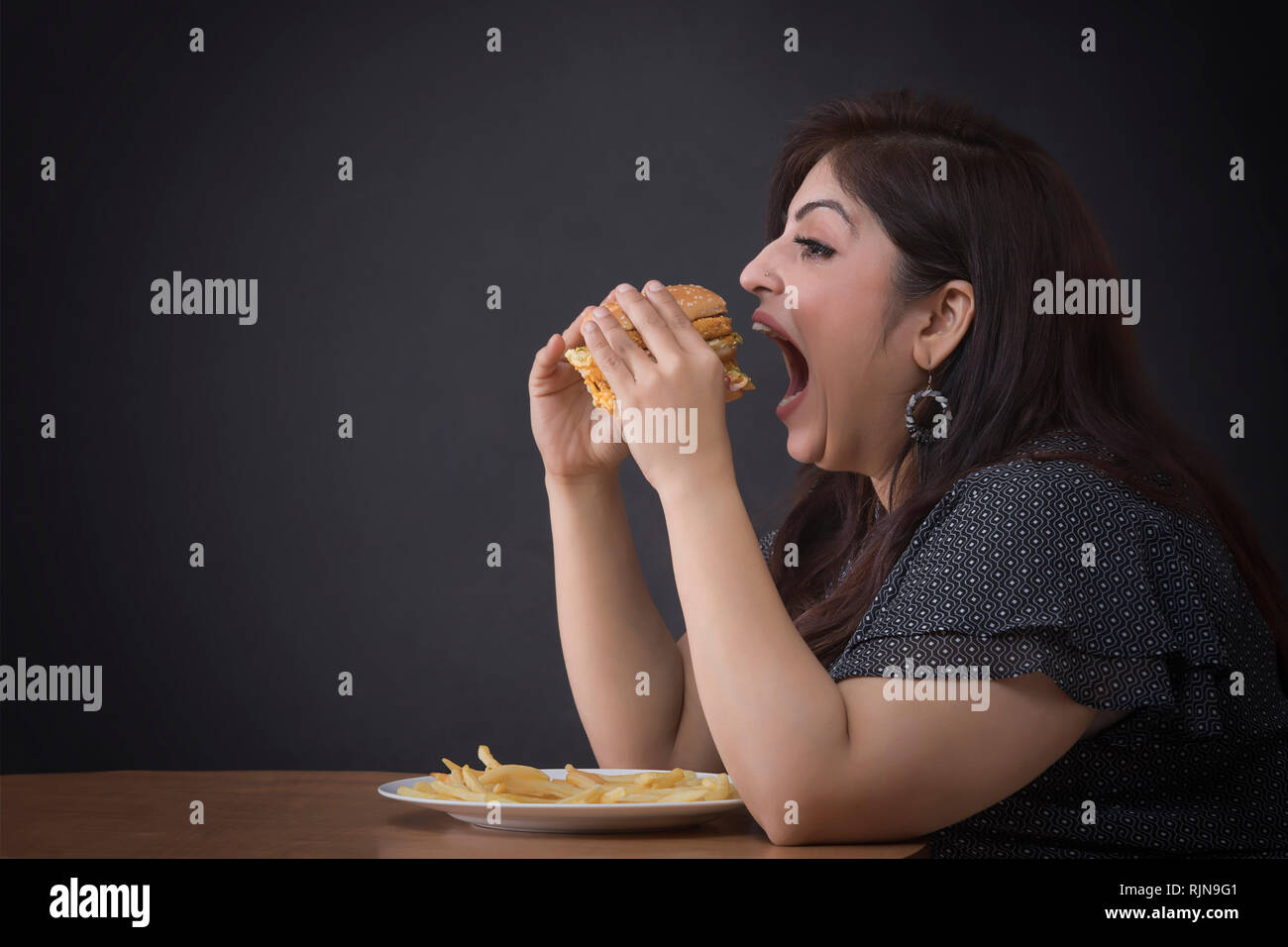 Donna grassa mangiare un hamburger Foto Stock