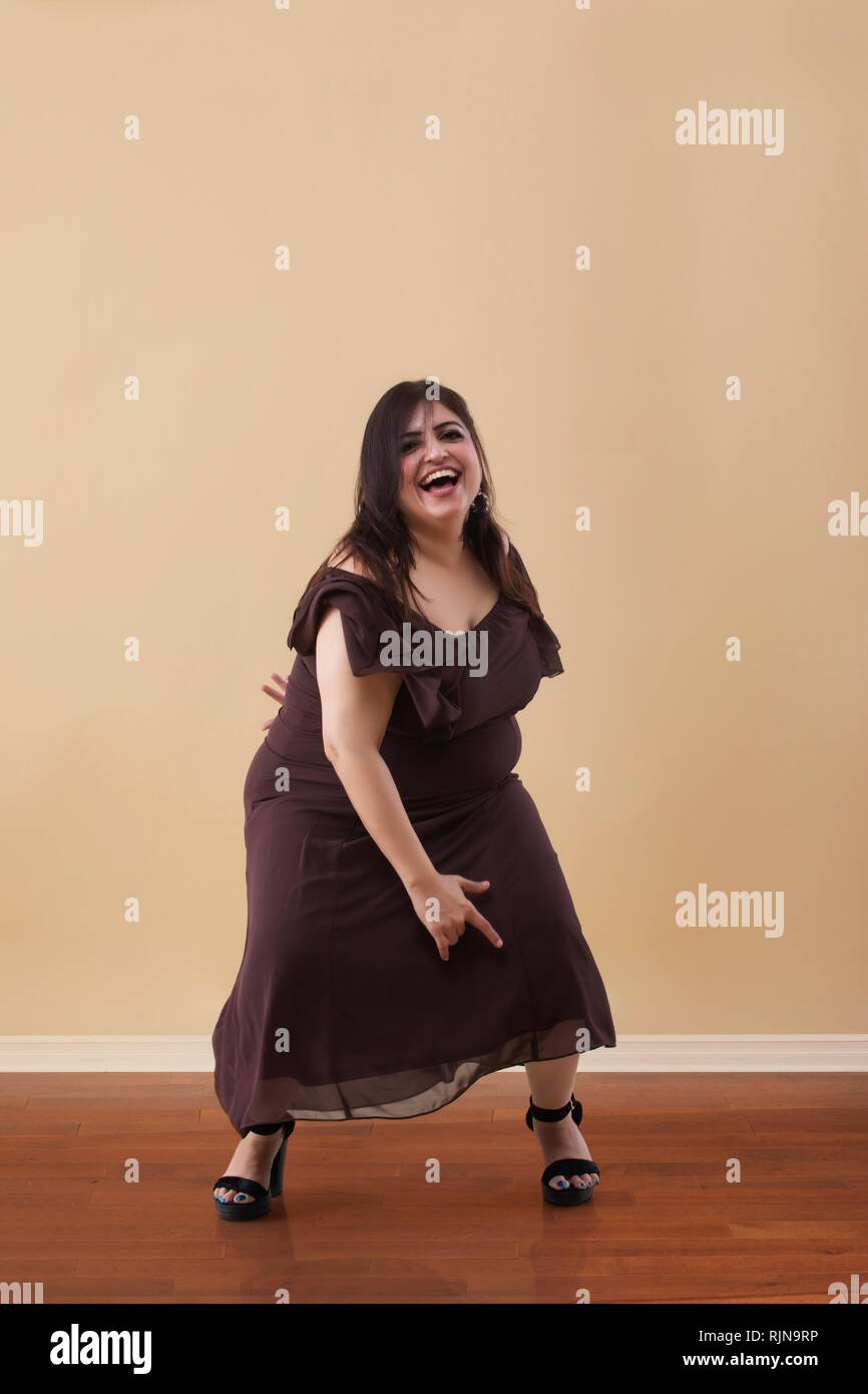 Donna grassa in un lungo abito marrone ballare su tacchi alti Foto Stock