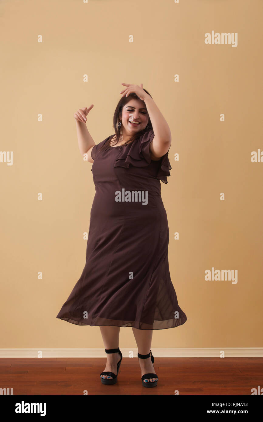 Donna grassa in un lungo abito marrone ballare su tacchi alti Foto Stock