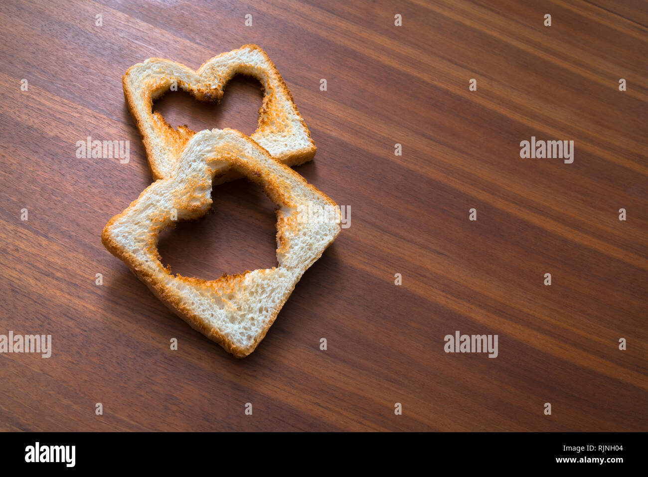 Tostare il pane bianco toast con la forma di cuore in legno marrone sfondo, amore, il giorno di san valentino Foto Stock