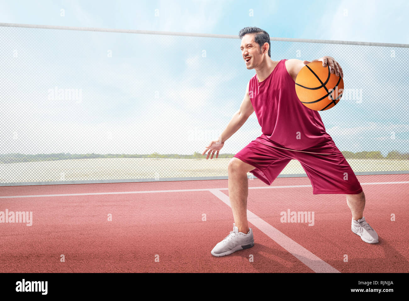 Allegro asian giocatore di basket uomo in azione con la palla all'aperto sulla pallacanestro Foto Stock