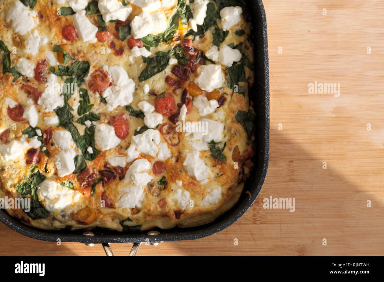 Un cucinata fresca frittata fatta con uova sbattute e formaggio di capra di pomodoro, basilico fresco. La sua ancora caldo nella padella utilizzata per cucinare Foto Stock