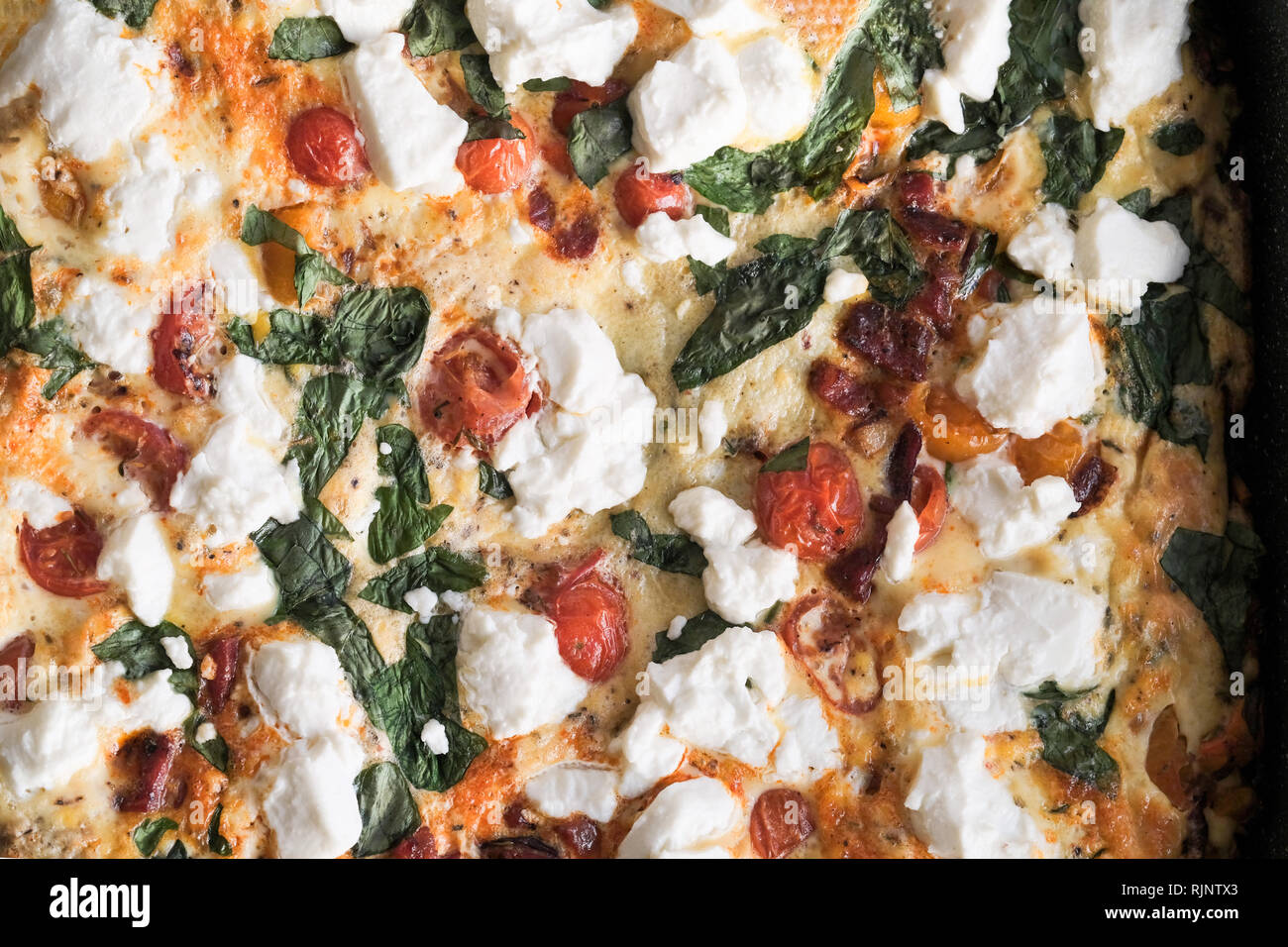 Un cucinata fresca frittata fatta con uova sbattute e formaggio di capra di pomodoro, basilico fresco. La sua ancora caldo nella padella utilizzata per cucinare Foto Stock