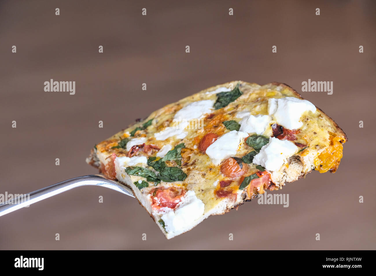 Un cucinata fresca frittata fatta con uova sbattute e formaggio di capra di pomodoro, basilico fresco. La sua ancora caldo nella padella utilizzata per cucinare Foto Stock
