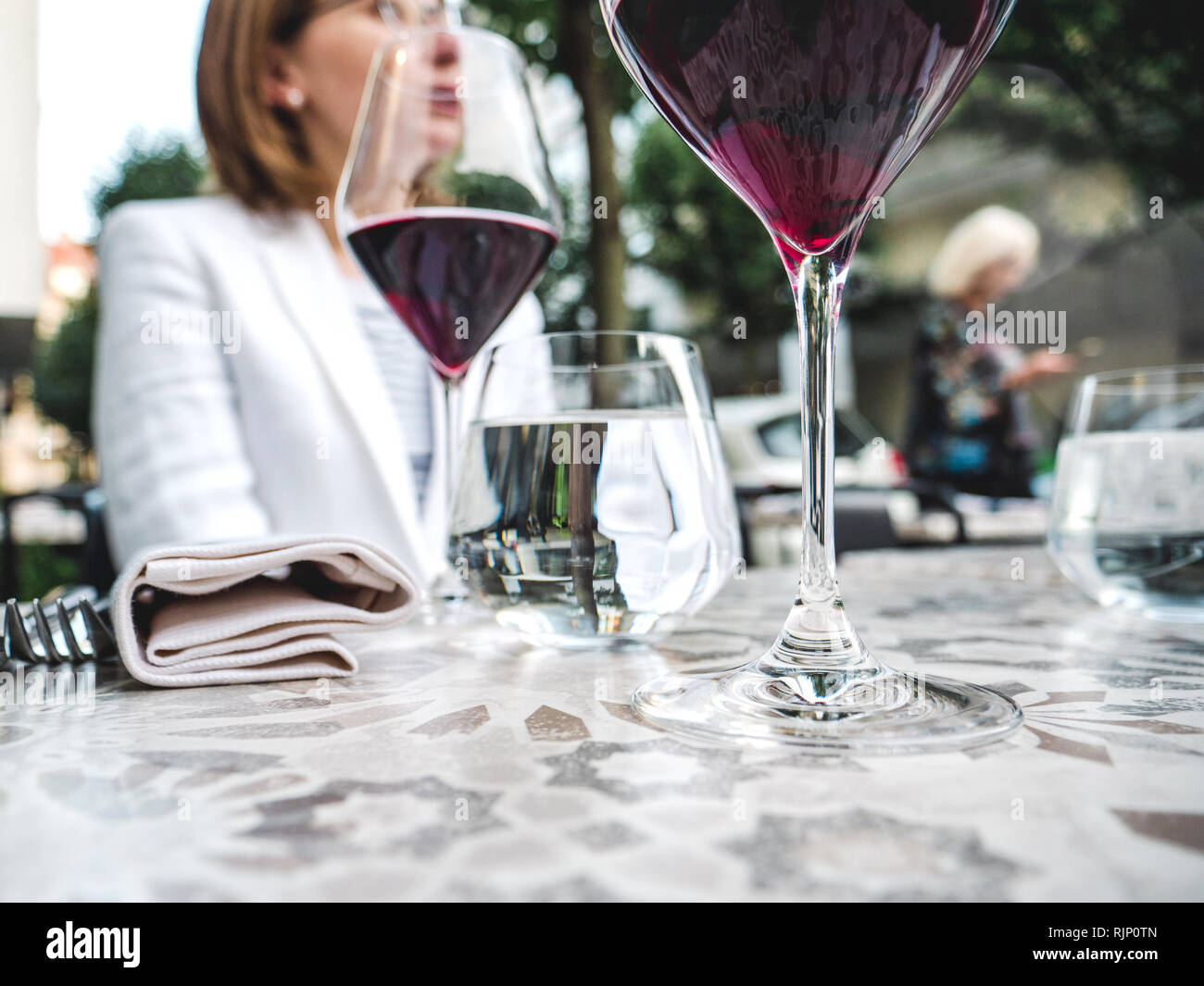 Closeup shot di bicchieri di vino rosso e acqua sul tavolo nel ristorante  con donna seduta su sfondo Foto stock - Alamy