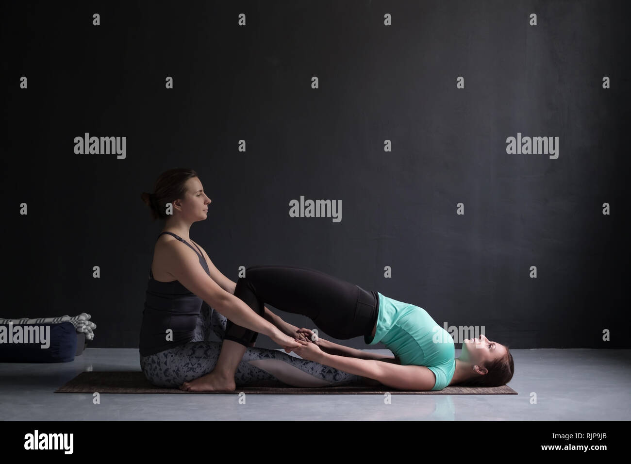 Giovane donna in ardha chakrasana yoga posa. Maestro aiutarla a farlo. Foto Stock