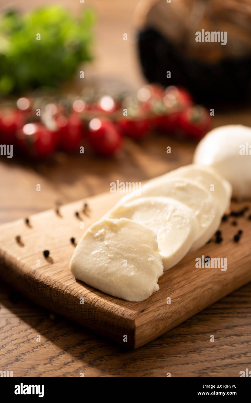 Mozzarella sul tagliere di legno. Pomodori ciliegia in background. Tavolo in legno con il cibo italiano composizione Foto Stock