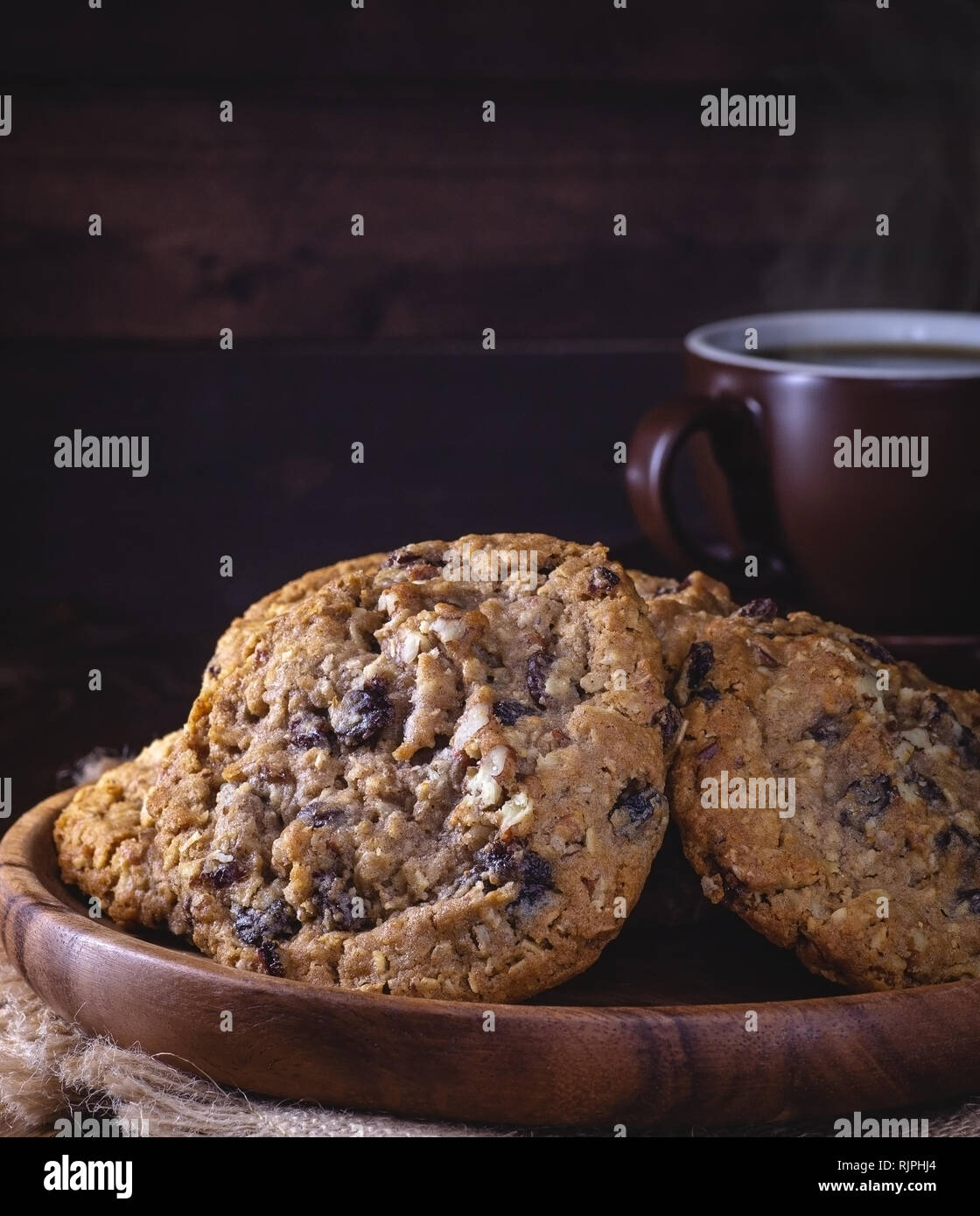 Primo piano di una pila di fiocchi d'avena dado raisin cookies sul piatto di legno e una tazza di caffè al buio su un sfondo di legno con spazio di copia Foto Stock