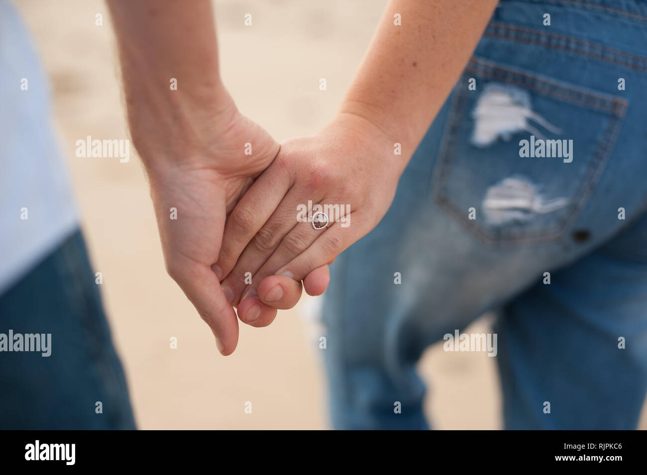 Posizione orizzontale vicino la fotografia di una giovane coppia tenendo le mani sulla spiaggia con il focus sull'anello durante un servizio fotografico presso la spiaggia in un giorno nuvoloso. Foto Stock