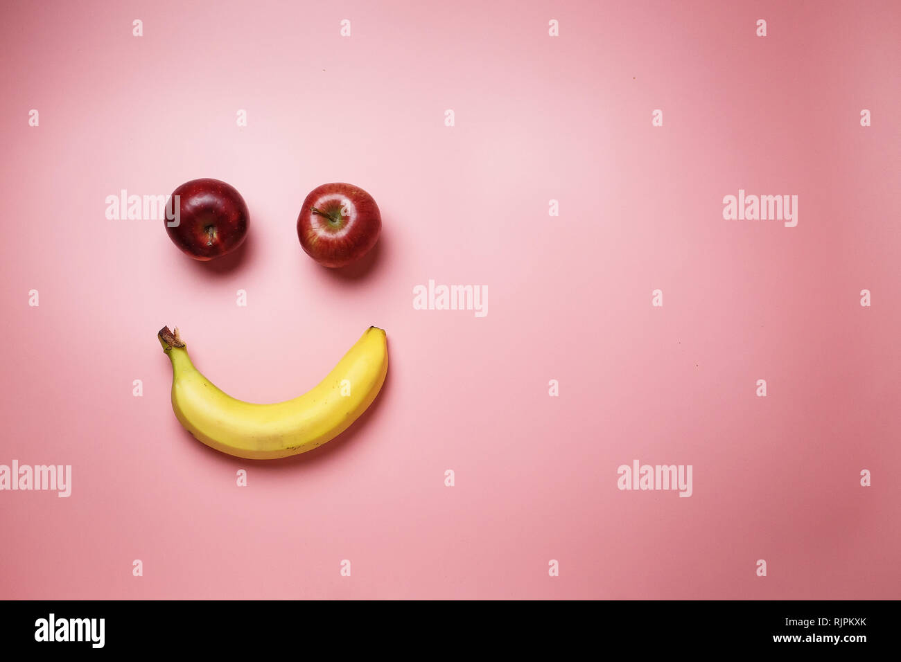 Banane e mele smiley rosa su sfondo di moda con spazio per il testo Foto Stock