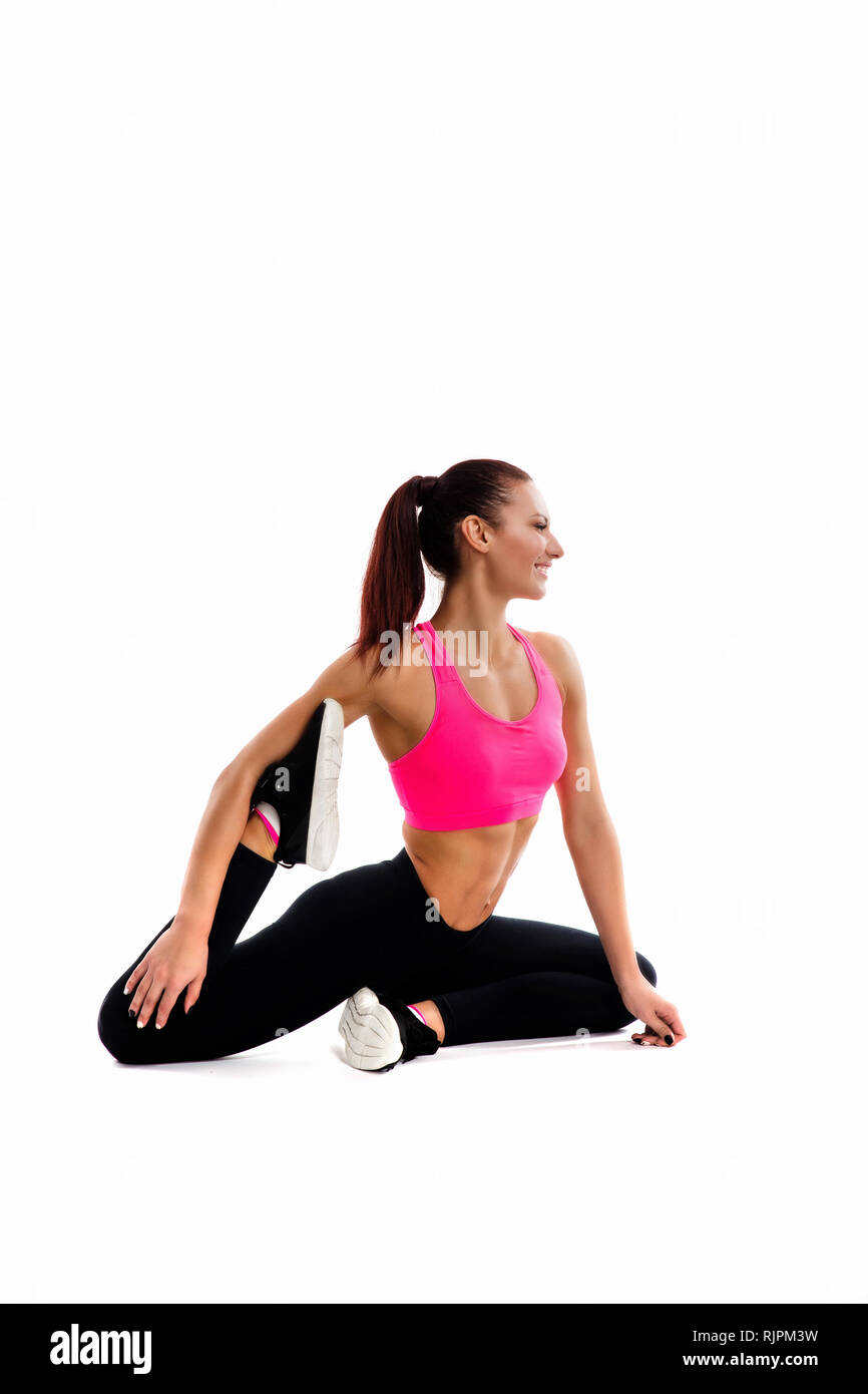 Giovane donna fitness facendo stretching le sue gambe. Foto di donna muscolare nel quartiere alla moda di abbigliamento sportivo su sfondo bianco. Foto Stock