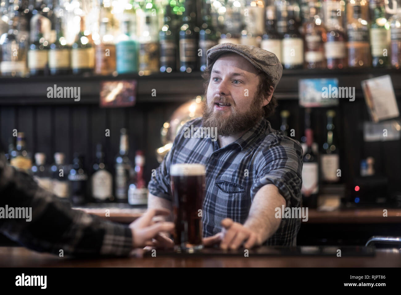 Il Barman che serve birra al cliente al bar in irlandese tradizionale casa pubblica Foto Stock