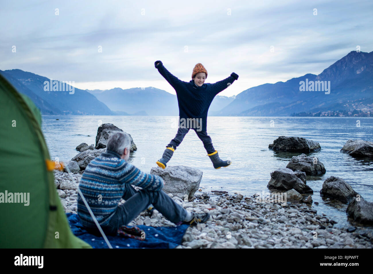 Padre guardando figlio facendo star jump Via Lungolago, Onno, Lombardia, Italia Foto Stock