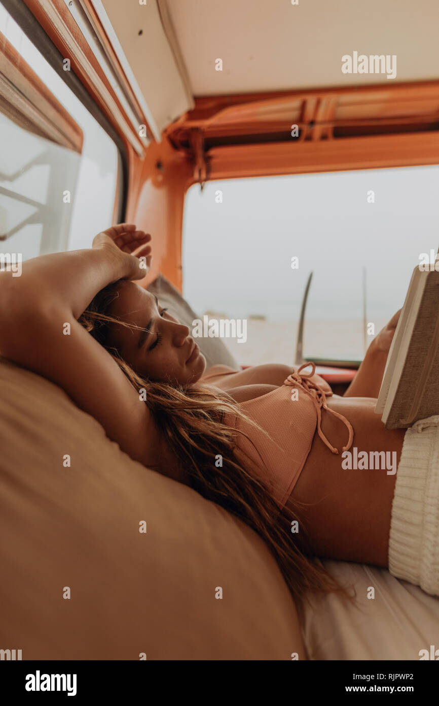 Giovani femmine surfer libro di lettura nel retro del veicolo per attività ricreative in spiaggia, Jalama, CALIFORNIA, STATI UNITI D'AMERICA Foto Stock