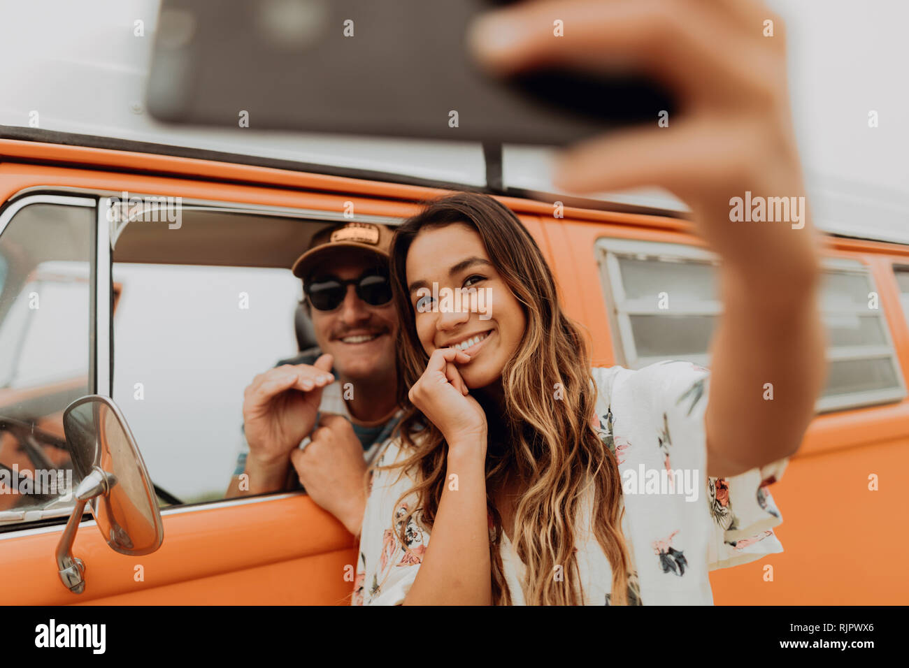 Una giovane coppia in viaggio nel veicolo per attività ricreative tenendo selfie smartphone, ritratto, Jalama, CALIFORNIA, STATI UNITI D'AMERICA Foto Stock