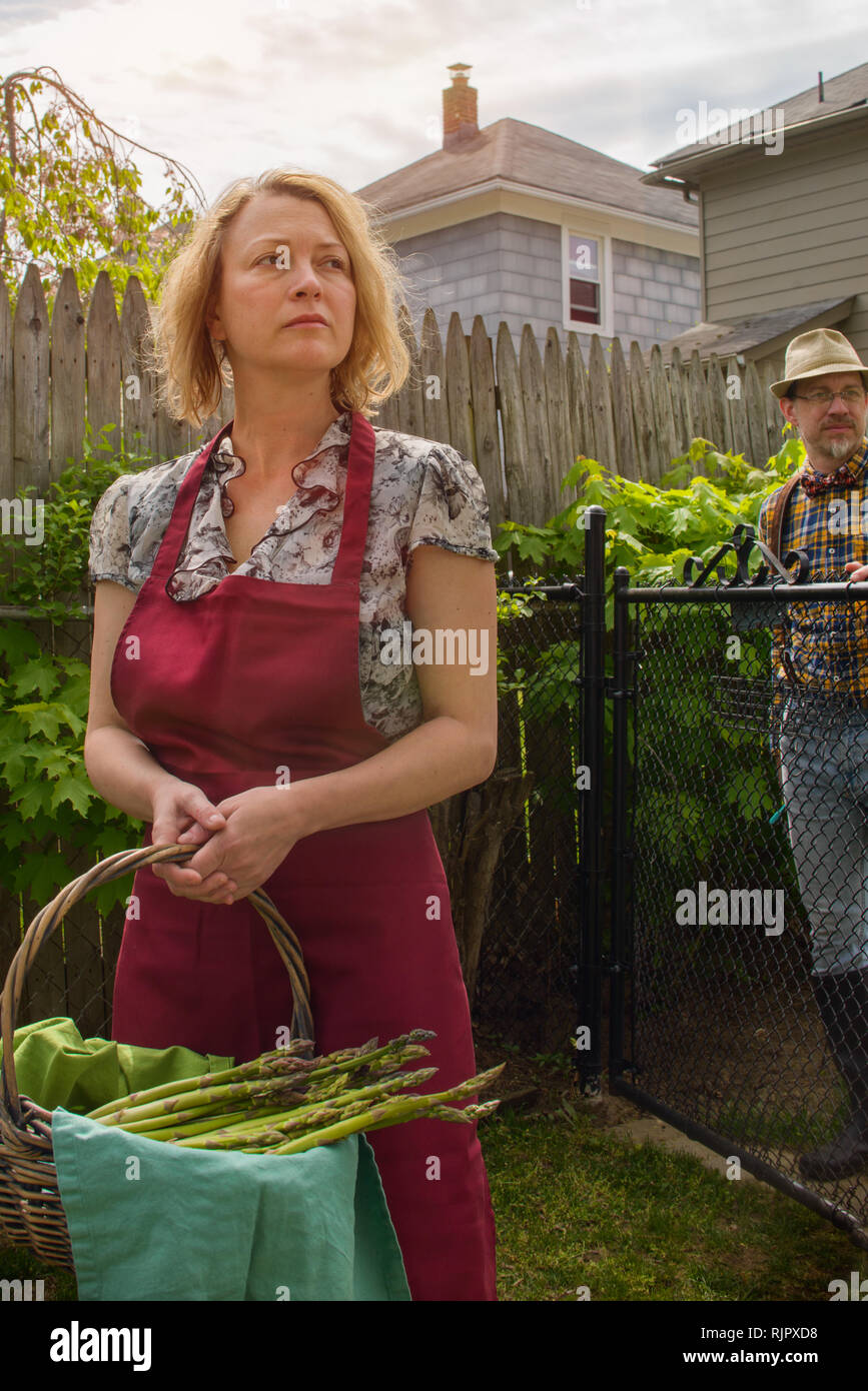 Donna con cesto di asparagi e marito distratti in giardino Foto Stock