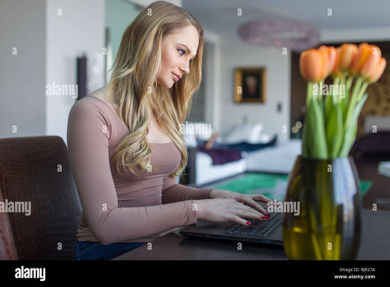 Donna bionda digitando su laptop in ambienti chiusi, comunicazione online Foto Stock