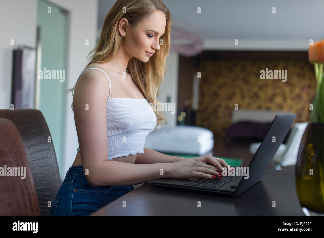 Giovane donna bionda digitando su laptop al chiuso in casa Foto Stock